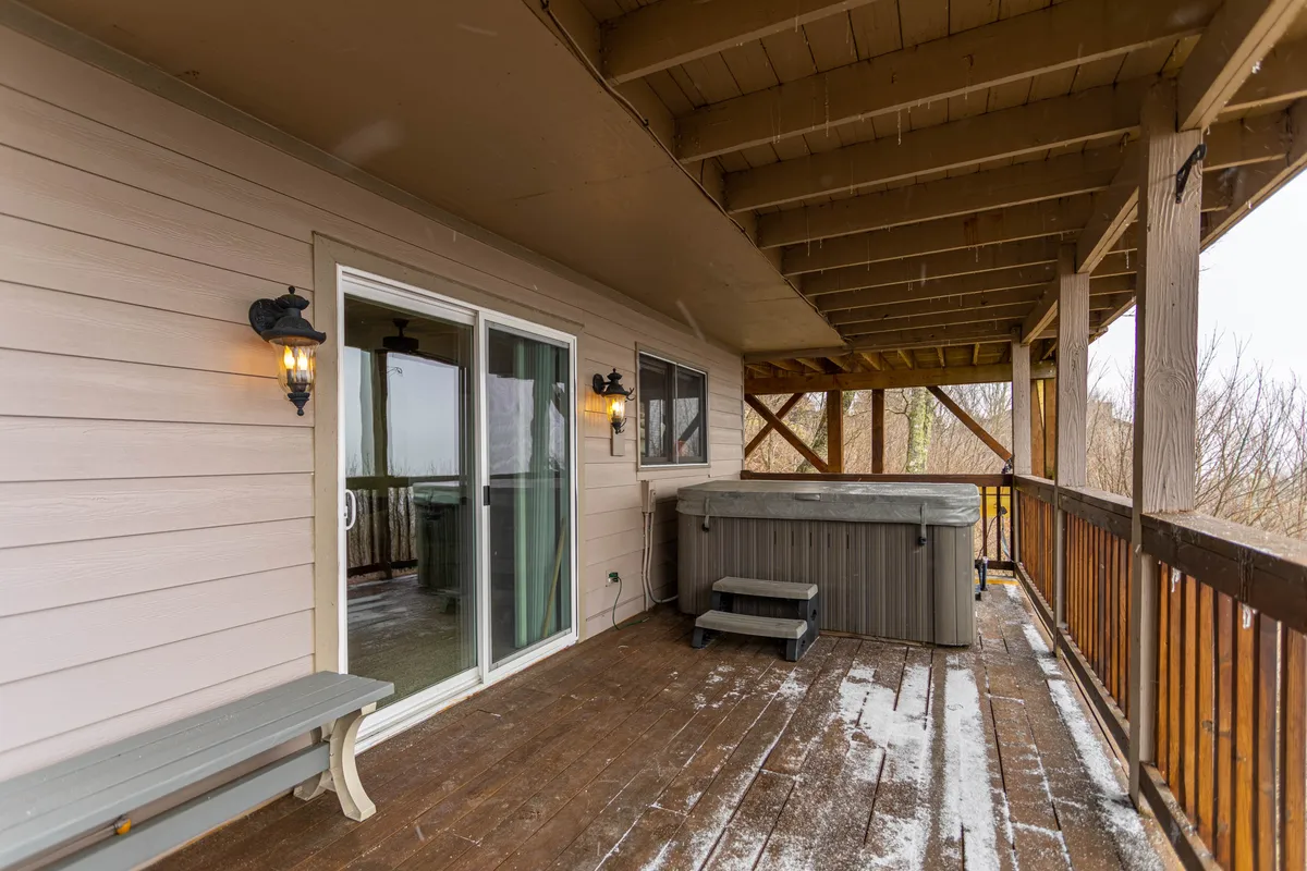 A calming exterior scene with a hot tub set on a wooden deck, framed by sliding glass doors and lush greenery. The inviting hot tub offers a relaxing vantage point for watching sunsets or stargazing after a day outdoors.