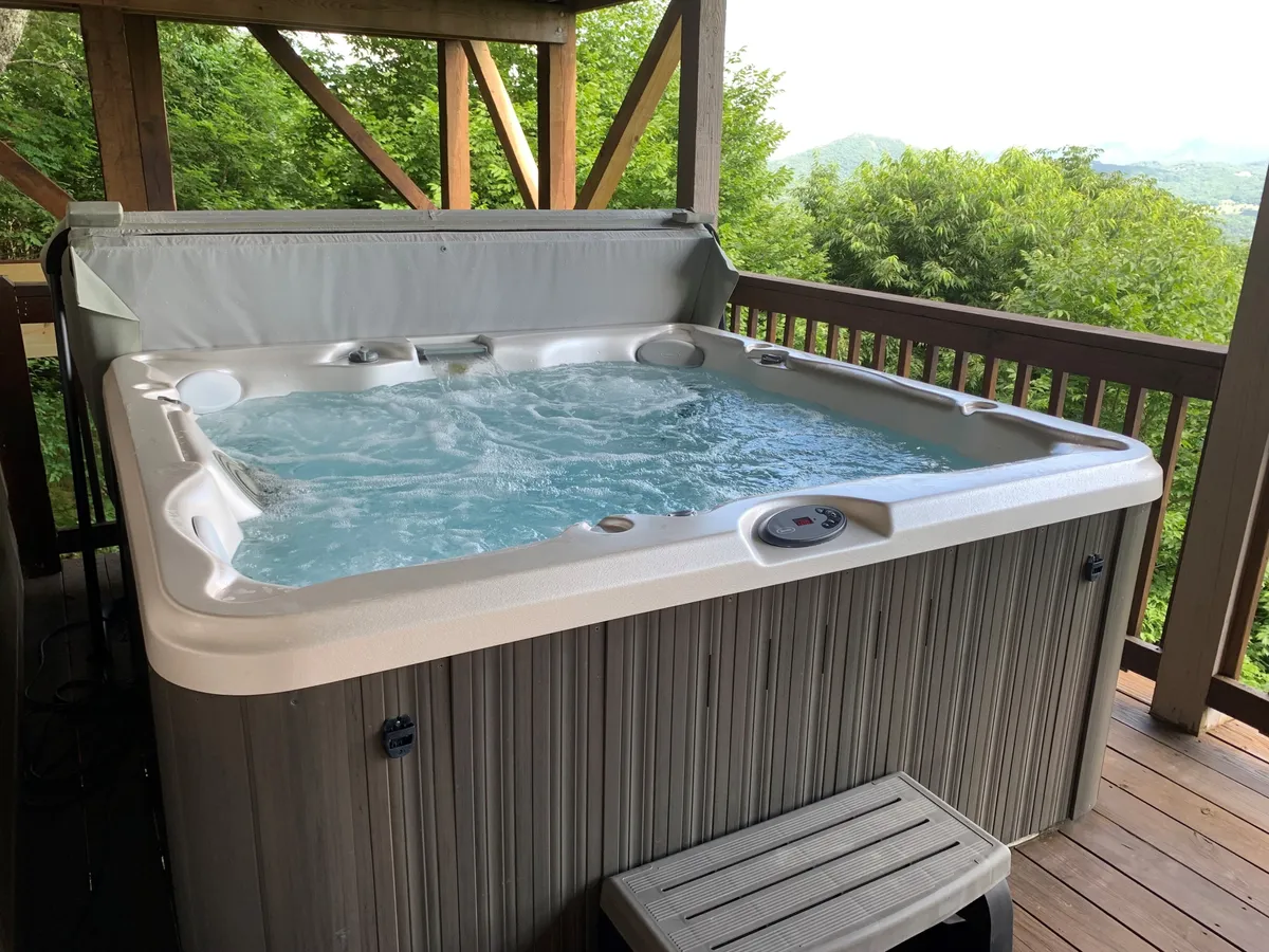 A private outdoor hot tub sits on a wooden deck, overlooking lush greenery. The inviting water promises a relaxing soak with scenic natural views, perfect for unwinding with a partner.