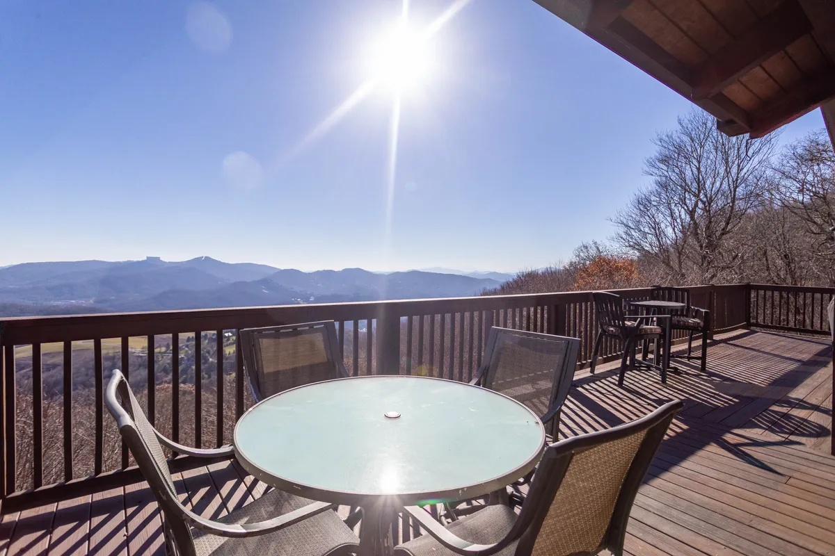 A serene outdoor dining set is arranged on the deck, overlooking a sweeping mountain view with sunlight streaming in. This space is ideal for al fresco meals, board games, or simply enjoying nature as a group, capturing the essence of shared experiences.