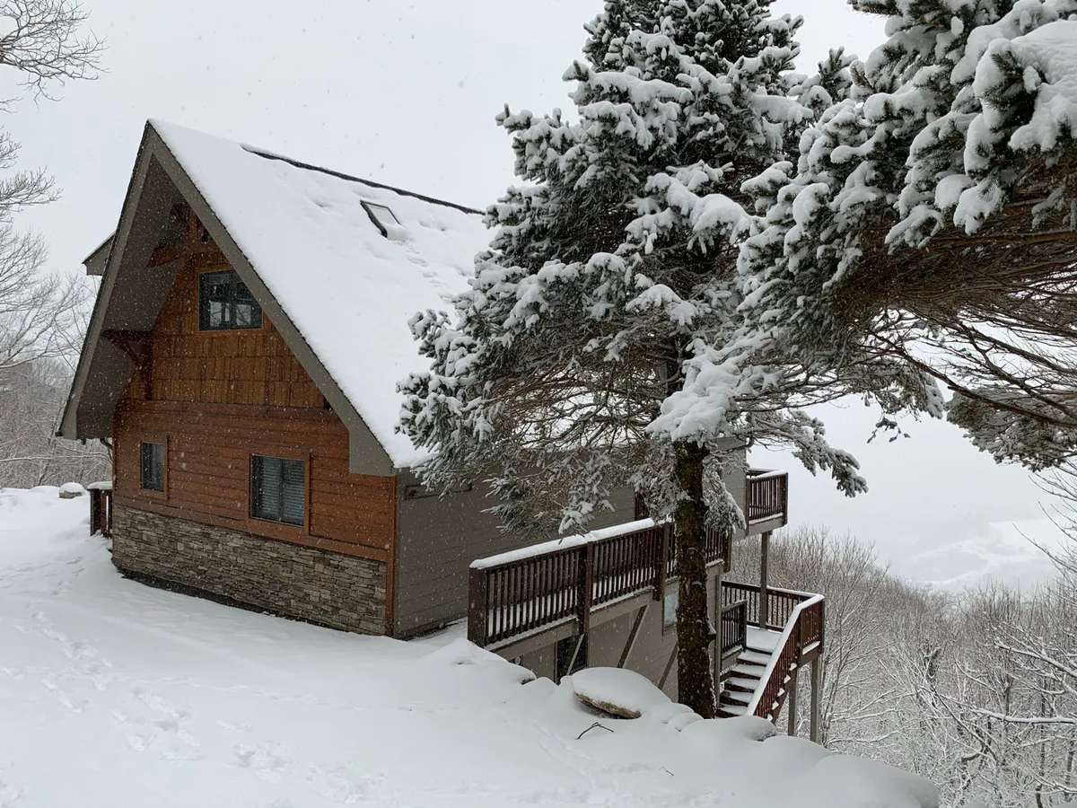 A snow-covered roof and wooden deck nestled among tall evergreens create a tranquil winter scene. This image evokes the excitement of winter adventures, snow activities, and cozy fireside gatherings mentioned in the section.
