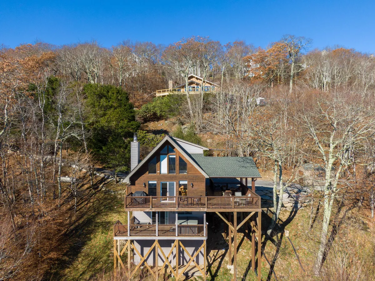 This image shows the wooden cabin with a large deck surrounded by trees, inviting families and groups to gather for outdoor activities. The spacious deck provides ample room for group games, barbecues, and relaxing together, while the natural setting hints at the mountain adventures nearby.