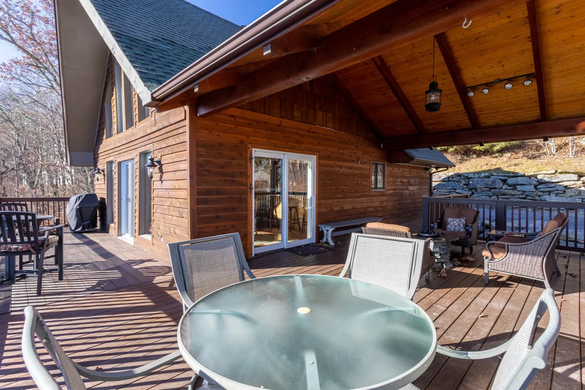 This image shows the main deck with an outdoor dining table and lounge seating, situated on a wooden deck with sliding glass doors leading inside. The space feels open and relaxed, ideal for alfresco meals and celebrations.