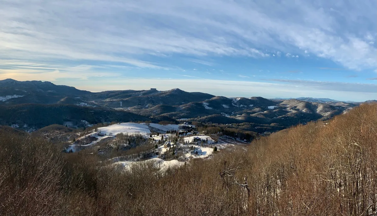 A sweeping vista shows snow-covered hills and distant mountain ranges beneath a vast blue sky. The scene evokes the vastness and tranquility of the High Country, inviting exploration and appreciation of the outdoors in all seasons.