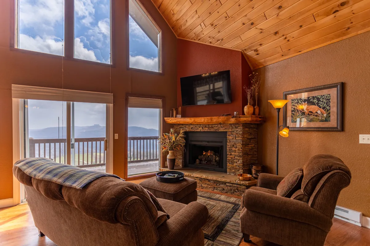 This interior image showcases a stone fireplace, large windows, comfortable seating, and decorative wall art. The area exudes warmth, with a relaxing and social atmosphere, suitable for intimate gatherings and watching movies.