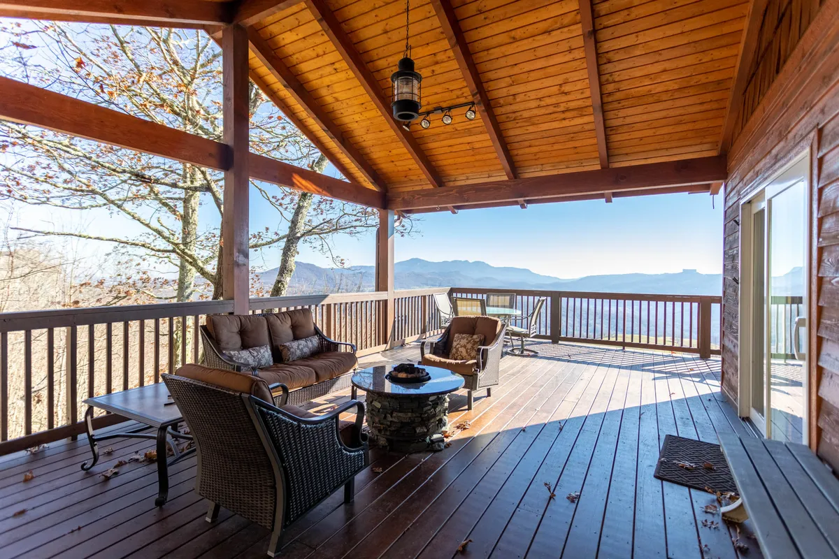 This exterior shot features a comfortable seating area and a fire pit, all set against the backdrop of majestic mountains. The mood is tranquil, inviting visitors to relax, chat, or enjoy the warmth of the fire table as the sun sets.